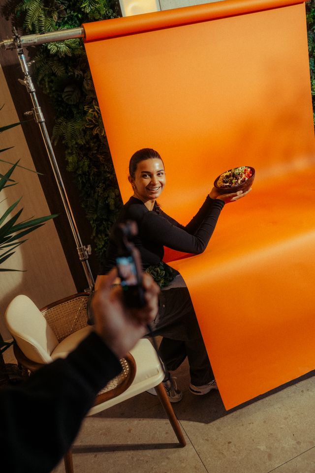 Een shoot van The Creative Guys: een model met een gerecht voor een oranje achtergronddoek, gefilmd met de telefoon.